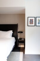 A modern hotel room with a large bed, a bedside table with a lamp, and two framed artworks on the wall.
