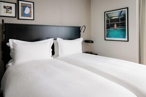 A hotel room with a large bed, two pillows, a headboard, a nightstand, a lamp, and framed pictures on the wall.
