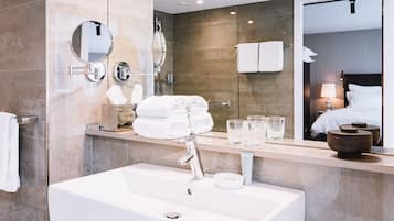 Un baño moderno con un lavamanos grande, dos espejos, una cabina de ducha de vidrio y toallas y artículos de aseo ordenados.