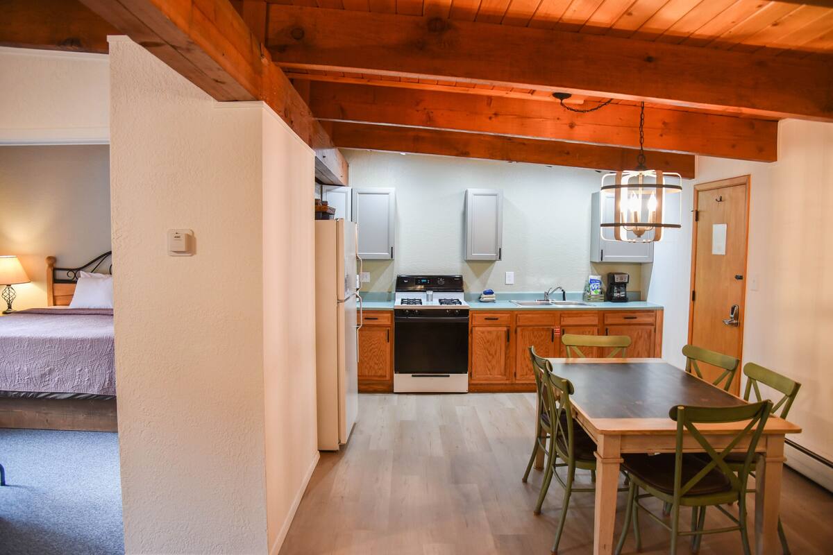 A compact kitchen with wooden cabinets, a stove, and a dining table with chairs.