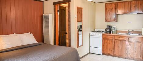A bedroom with a bed, a ceiling fan, and a kitchenette with wooden cabinets and a stove.