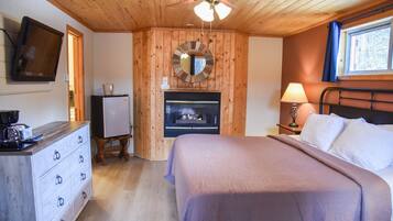 Een slaapkamer met een bed, een plafondventilator, een open haard, een televisie en een dressoir.