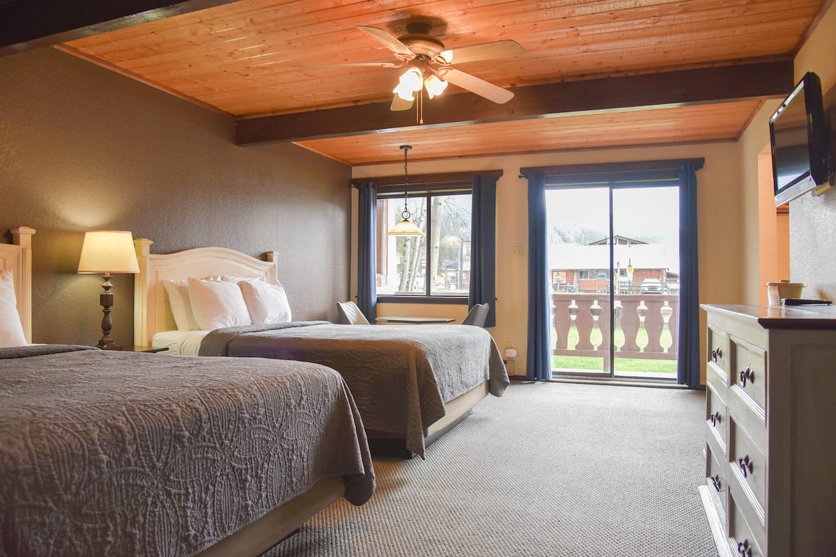 A hotel room with two beds, a ceiling fan, a TV, and a view of the outside.