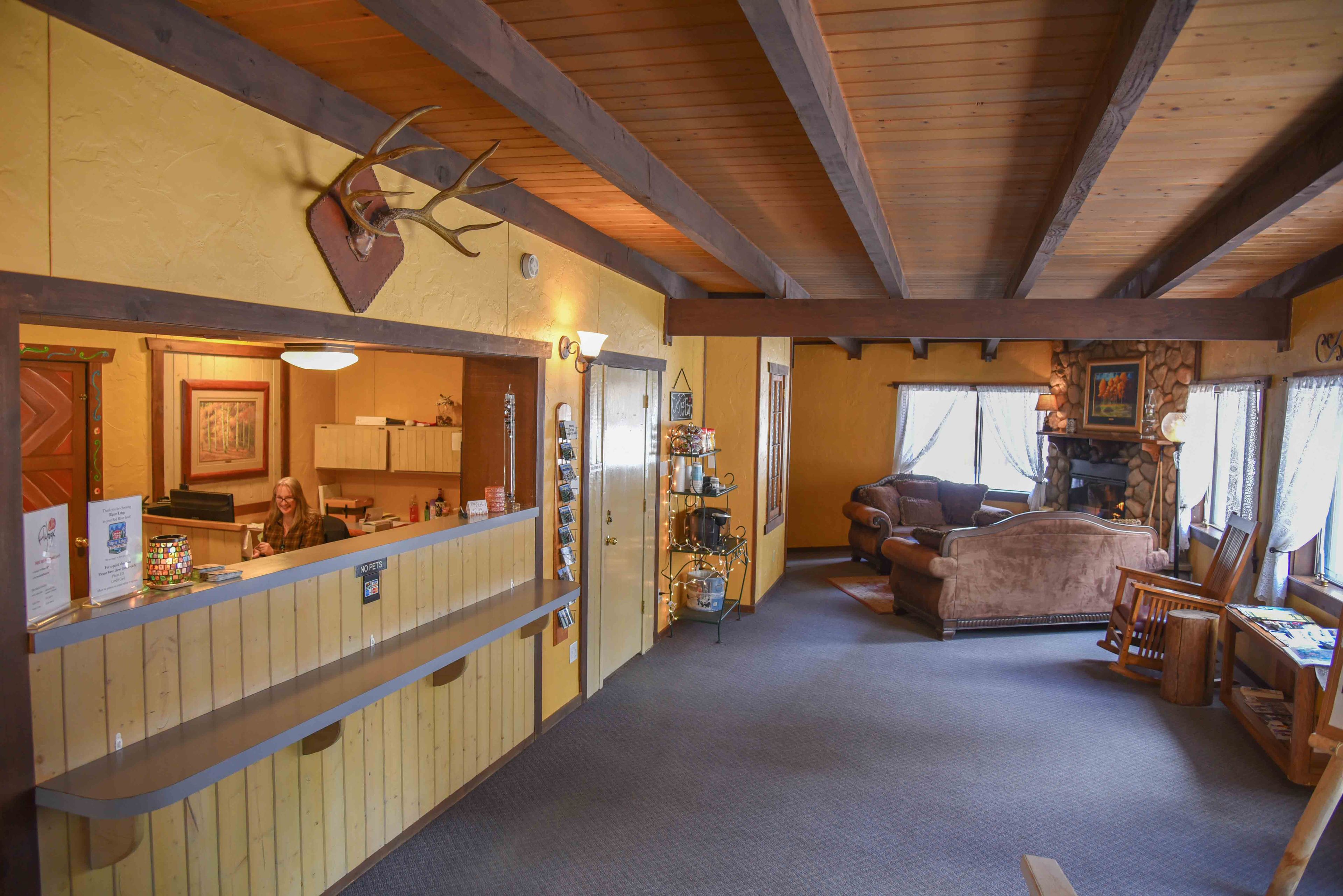 Uma área de recepção com balcão de madeira, um chifre montado na parede e uma sala de estar aconchegante com lareira.