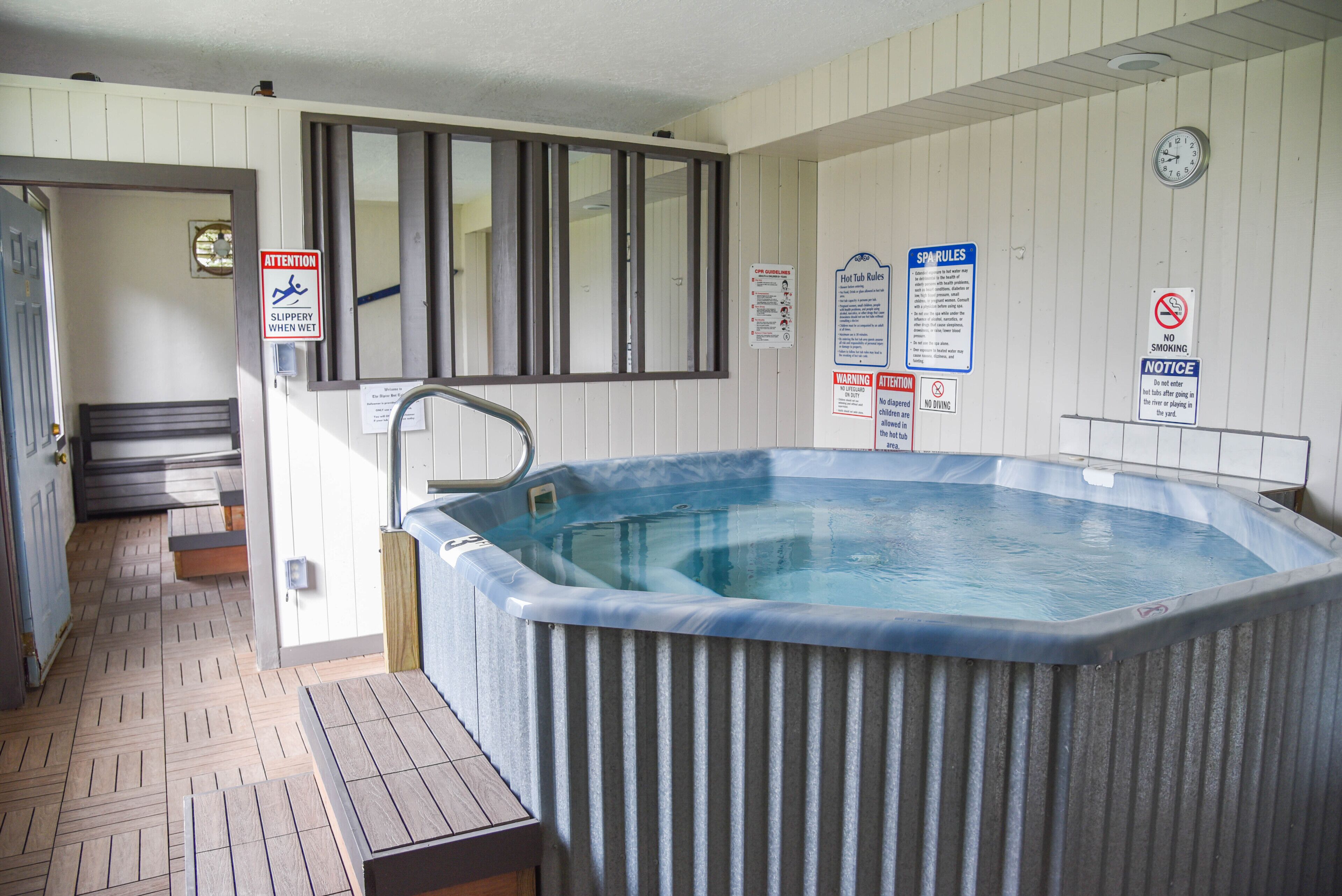 Un bain à remous dans une pièce dotée d’un plancher en bois, d’une fenêtre et de divers panneaux indiquant les règles de sécurité et les consignes relatives à l’utilisation des installations de bien-être.