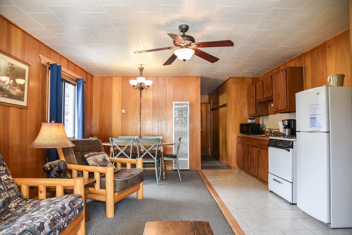 A compact kitchen with wooden cabinets, a white refrigerator, and a dining area with a table and chairs.