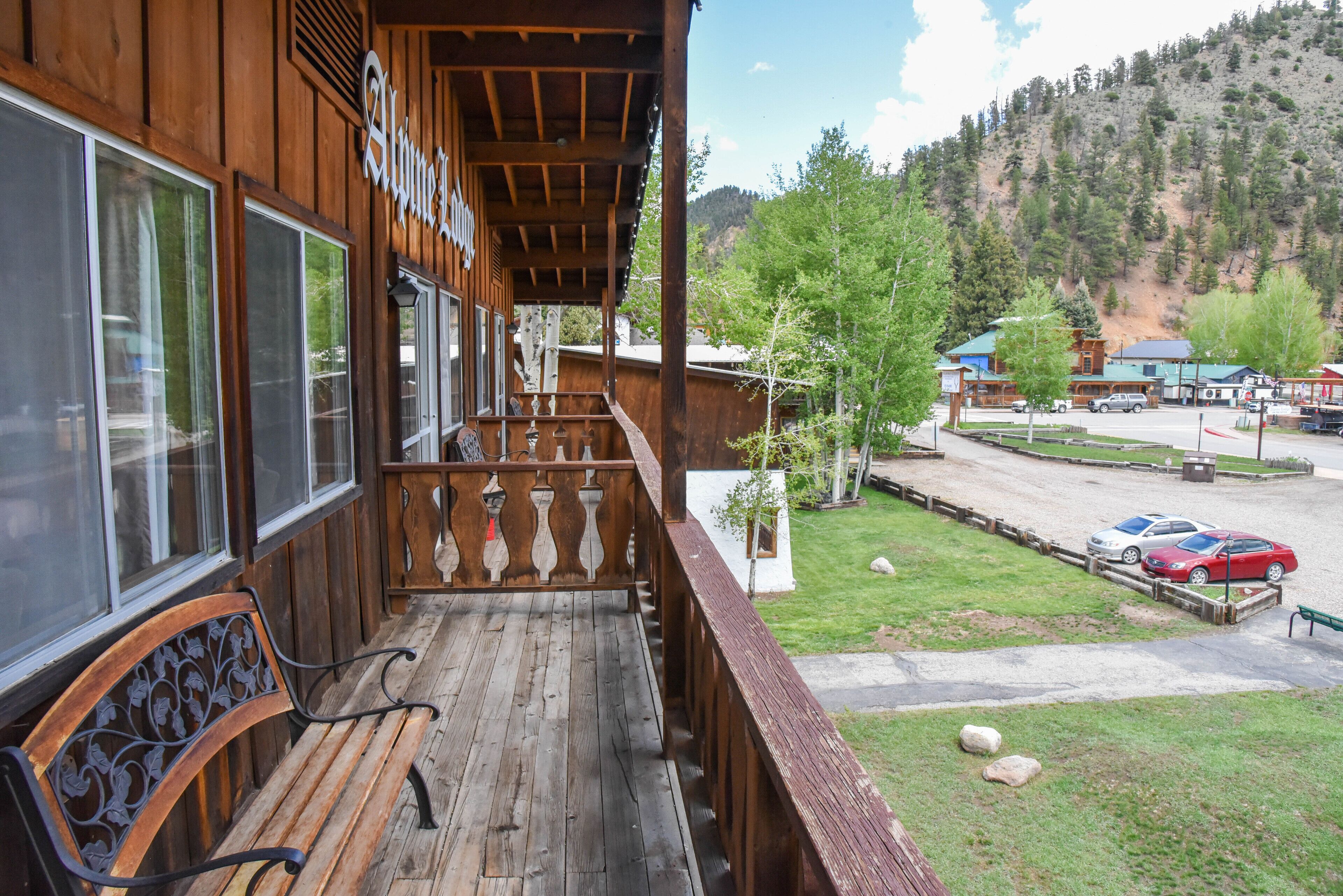 A wooden building with a balcony, a bench, and a view of a parking area and trees.