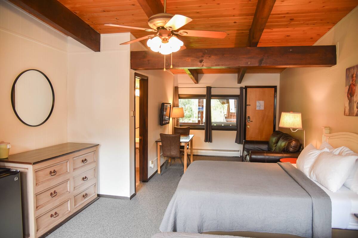 A hotel room with a bed, a desk, a chair, a dresser, and a ceiling fan.