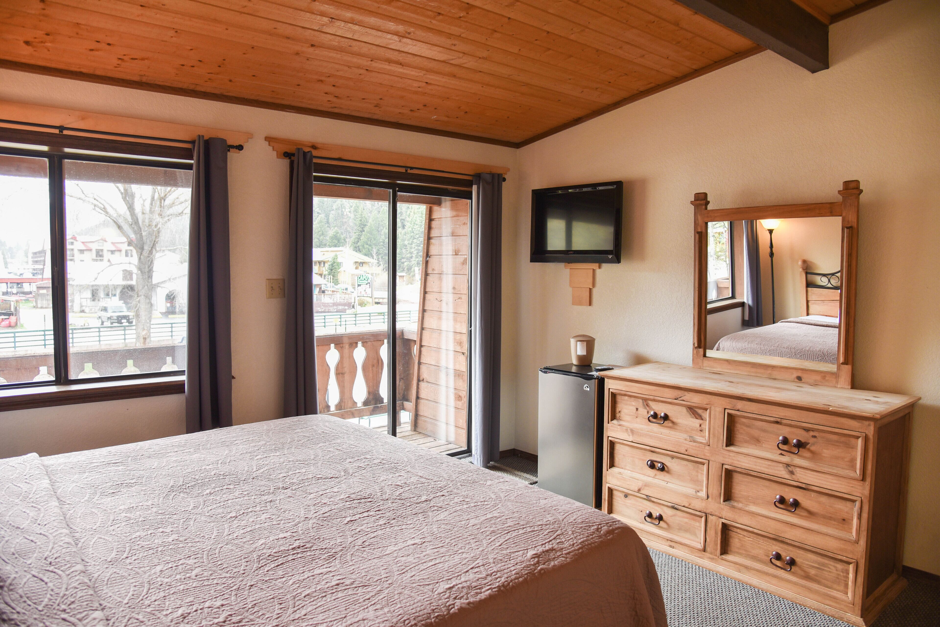 Un dormitorio con cama, cómoda de madera, televisor y un balcón con vistas al exterior.