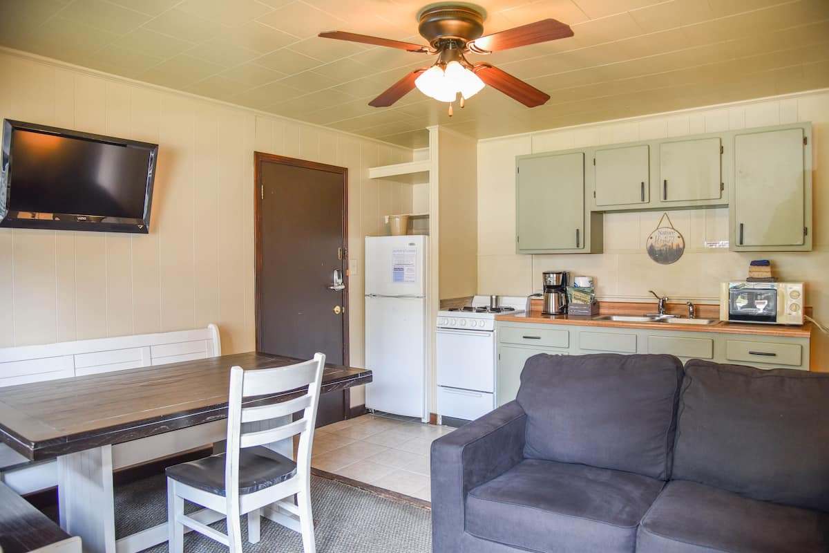 A compact kitchen with a dining table, chairs, a sofa, and a ceiling fan.