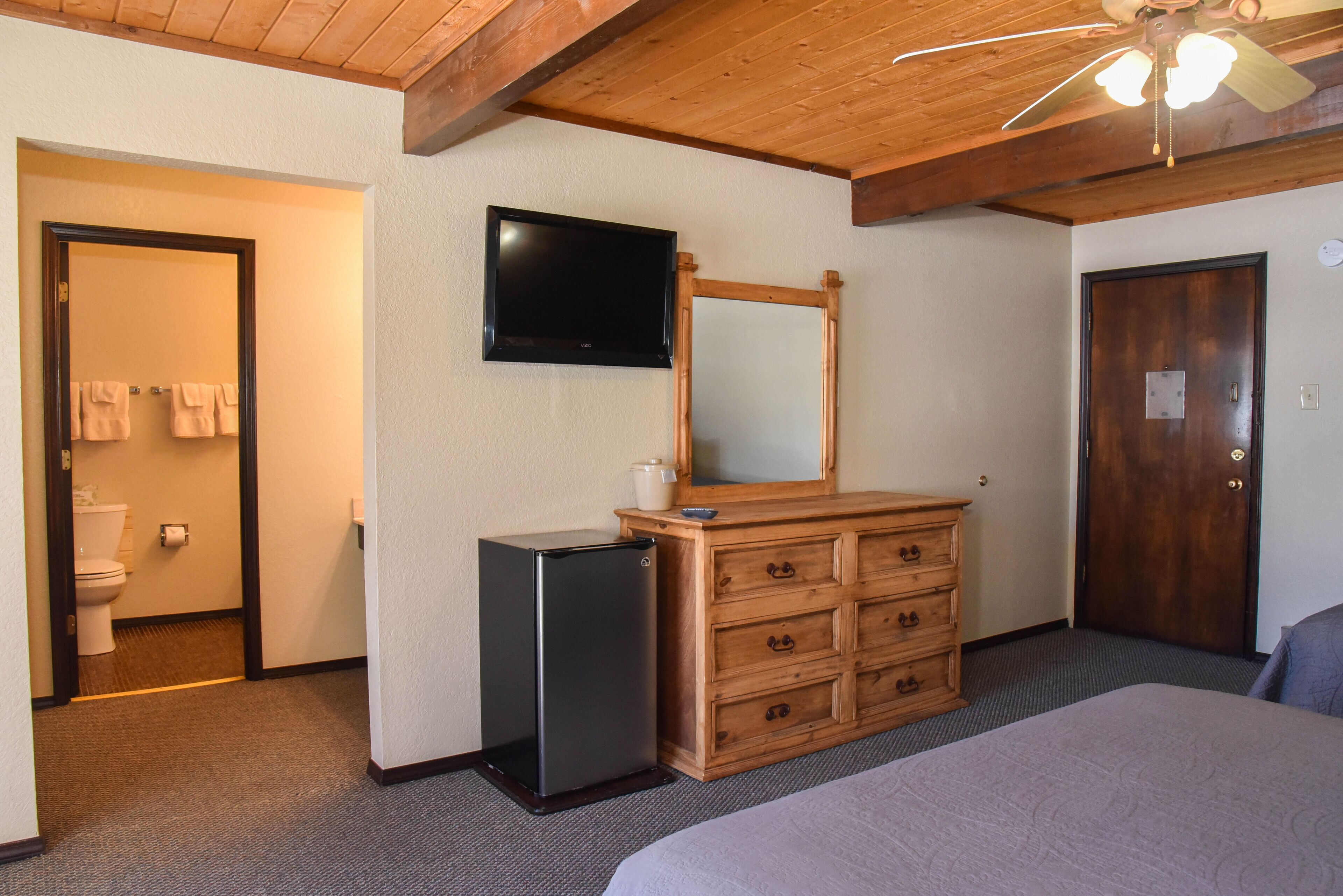 A bedroom with a bed, a wooden dresser, a television, and a ceiling fan.