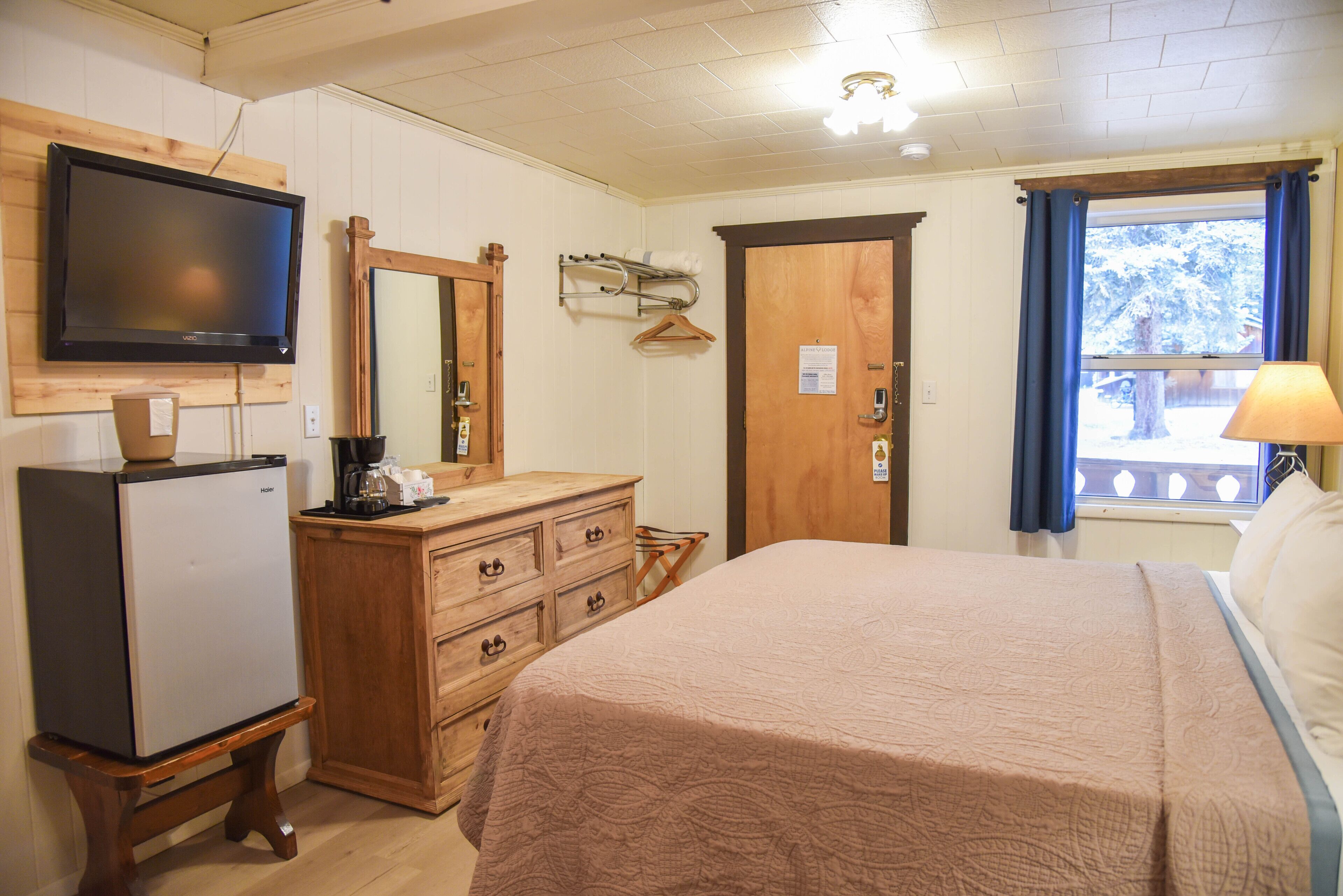 A bedroom with a bed, a dresser, a television, and a window with curtains.