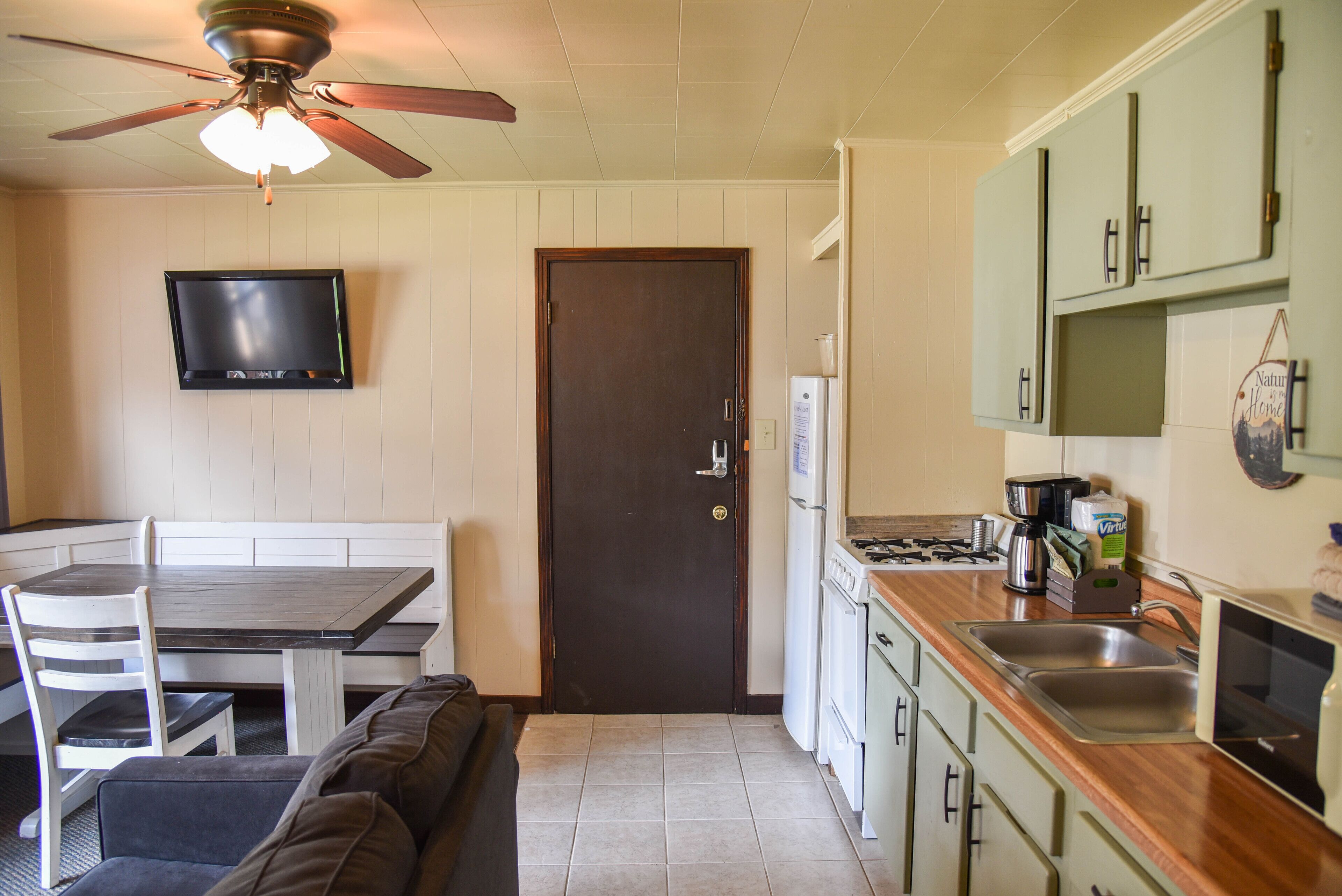 A compact kitchen with a dining area, a ceiling fan, a flat-screen TV, and green cabinets.