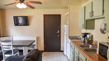 A compact kitchen with a dining area, a ceiling fan, a flat-screen TV, and green cabinets.