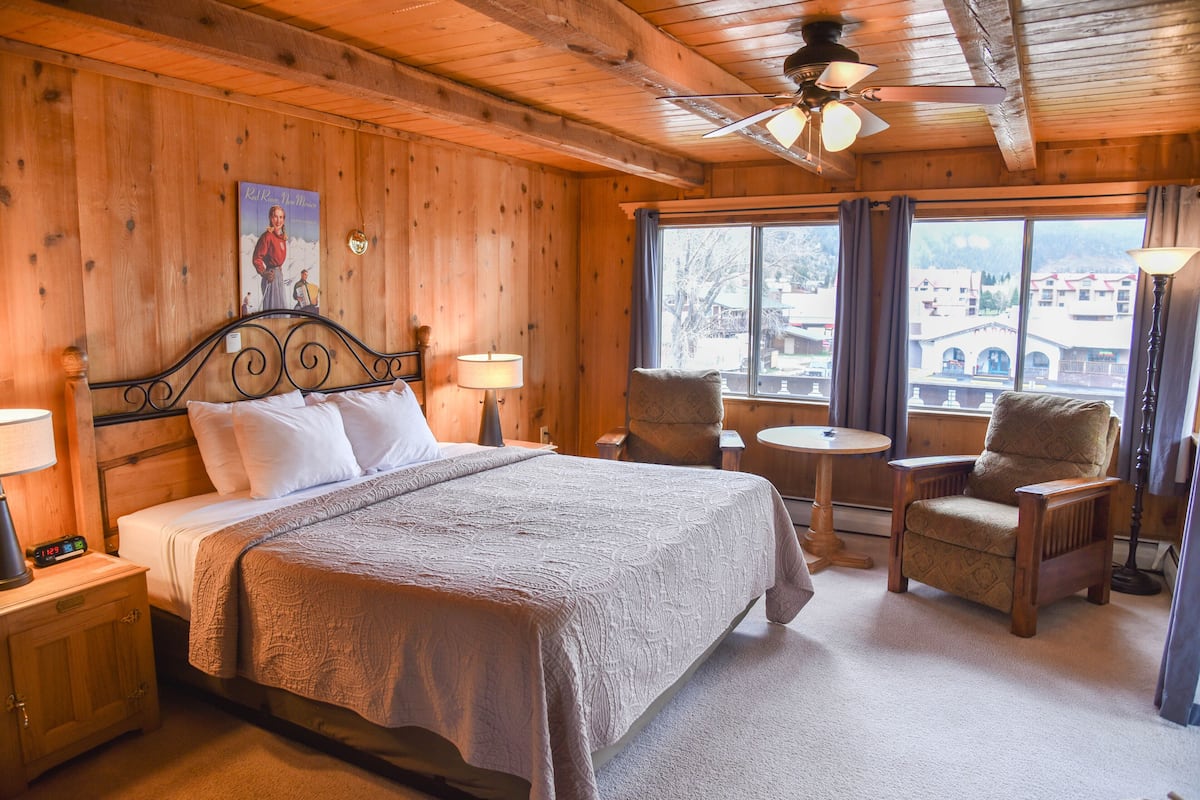 A wooden room with a bed, two chairs, a small table, and a window with a view.