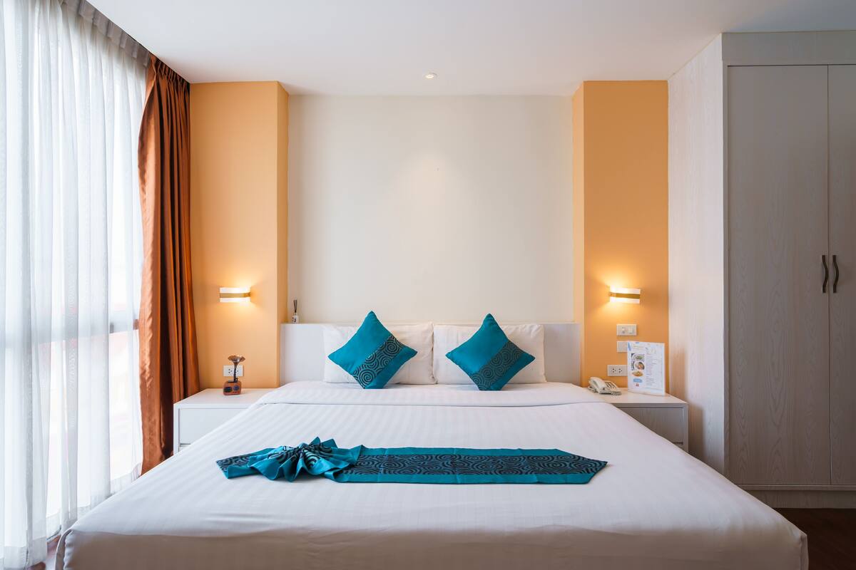 A hotel room with a large bed, two pillows, a bedside table with a lamp, and a wardrobe.