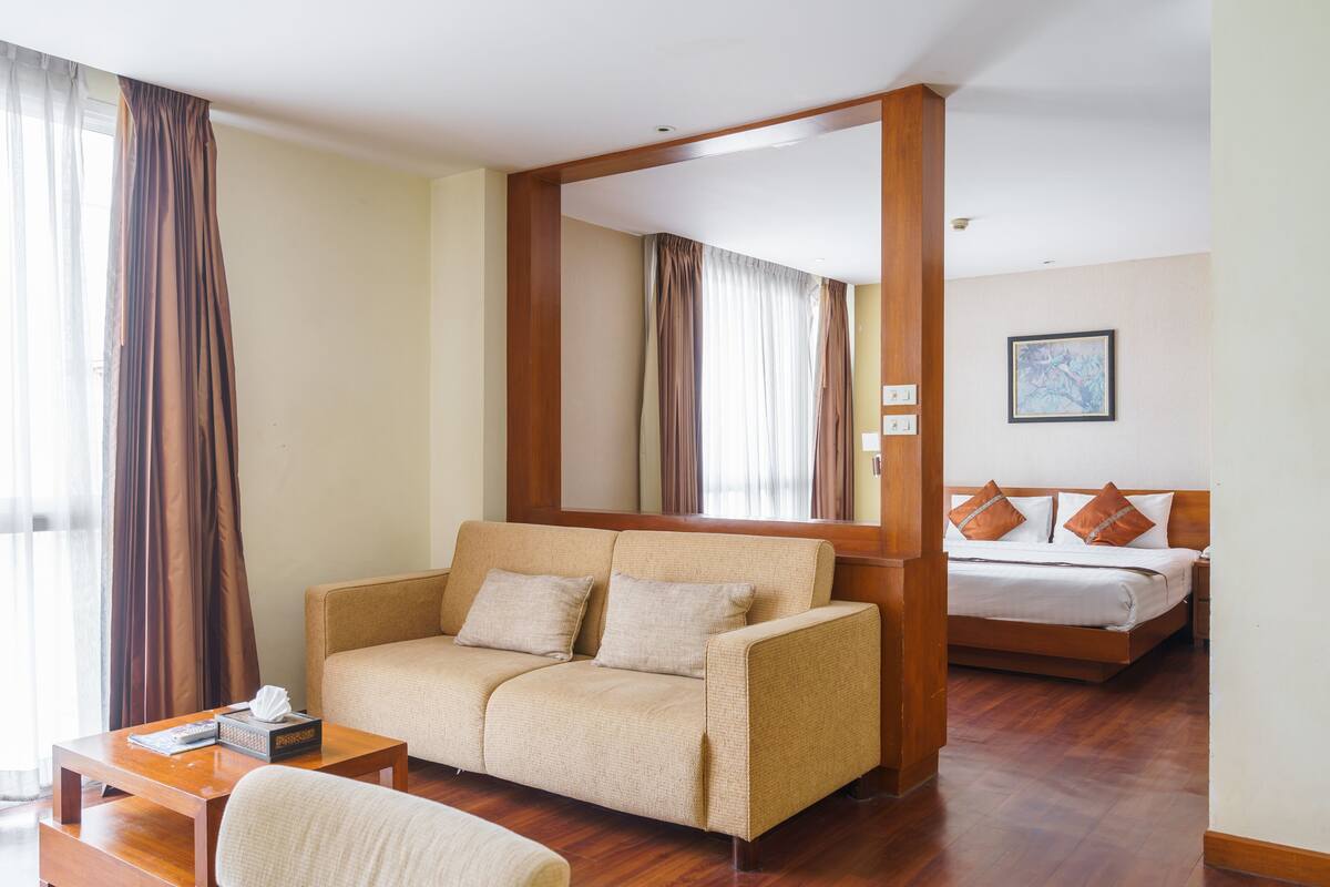 A hotel room with a sofa, a bed with pillows, a wooden floor, and a large mirror.