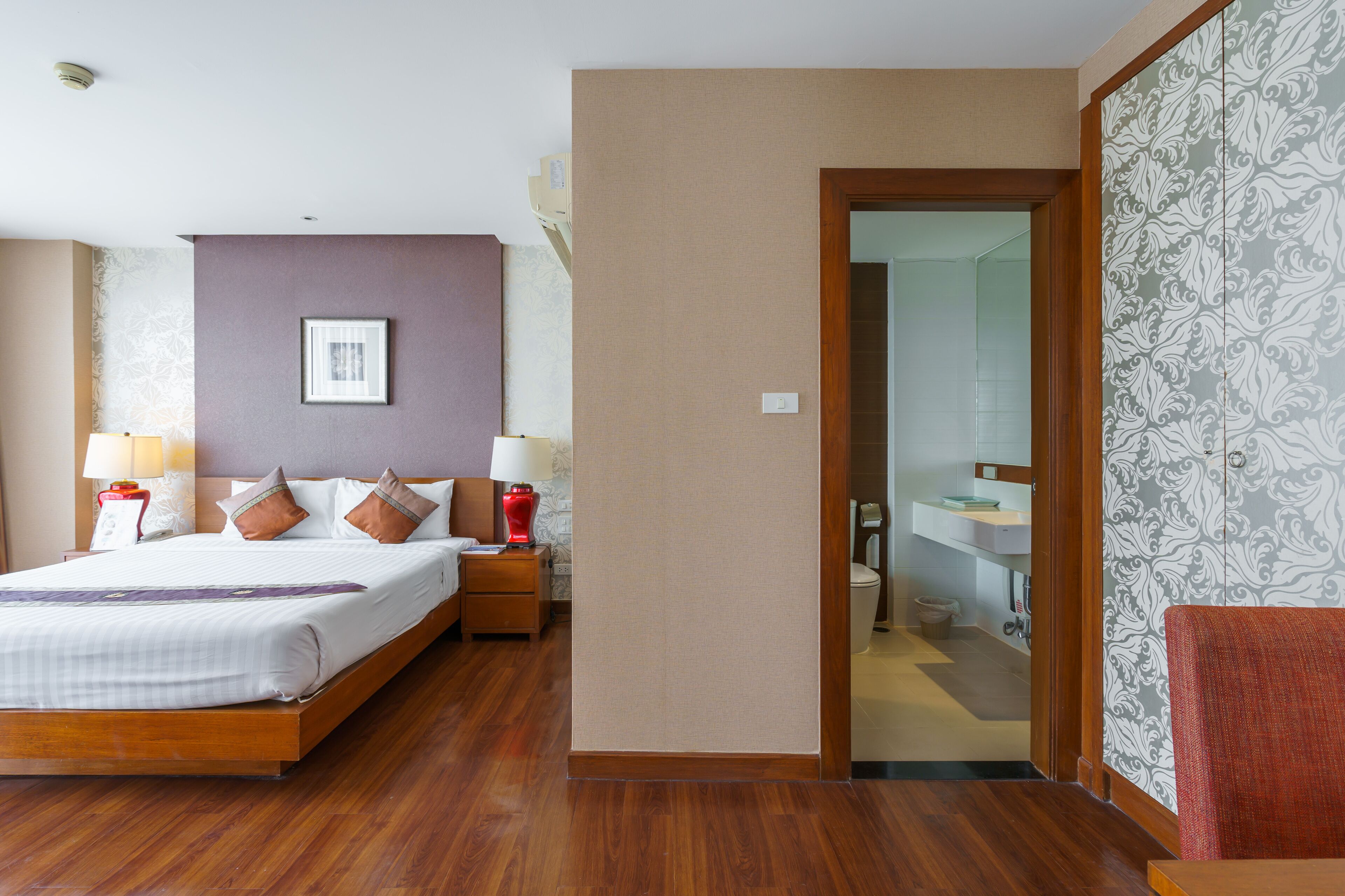 A hotel room with a wooden bed, two bedside tables with lamps, a framed picture on the wall, and a bathroom visible through an open door.