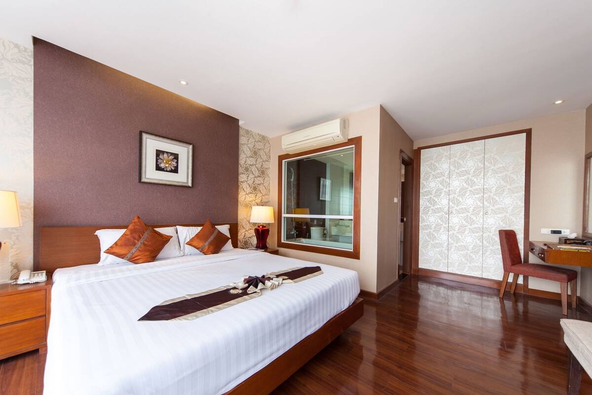 A hotel room with a large bed, a desk, a chair, and a wardrobe.