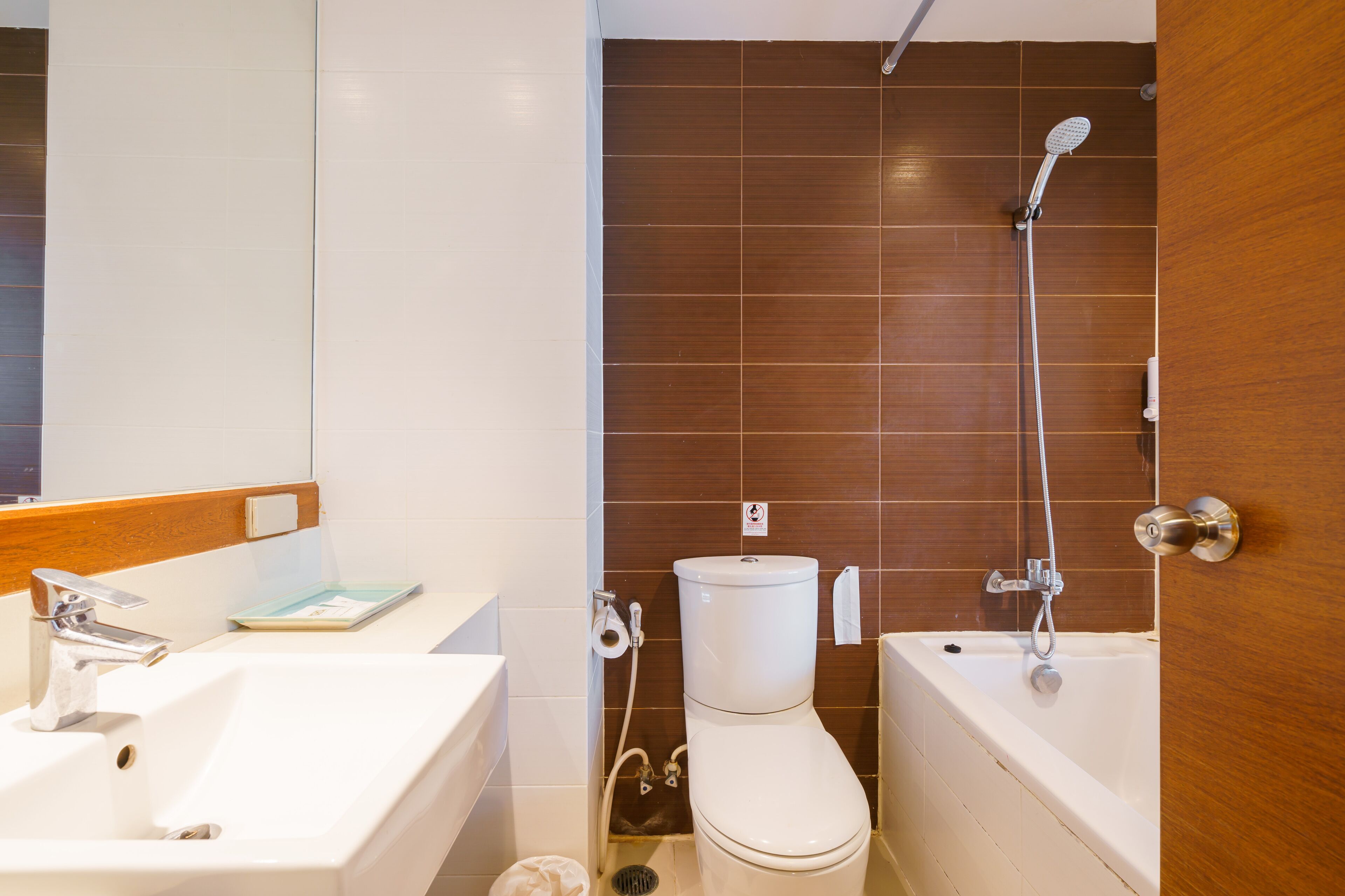 A bathroom with a white sink, toilet, and bathtub, wooden paneling on the walls, and a mirror above the sink.