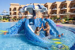 A water slide with a blue and white design, surrounded by a pool area with lounge chairs and umbrellas.