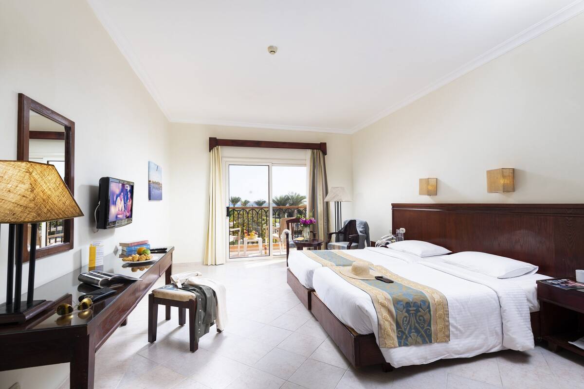 A hotel room with a bed, a desk with a lamp, a chair, a TV, and a view of the outdoors.