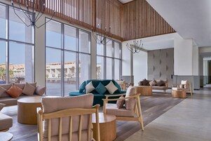 A spacious lobby with large windows, a green sofa, wooden chairs, and a modern chandelier.
