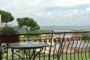 Un balcón con una mesa redonda, vista al mar y un árbol.