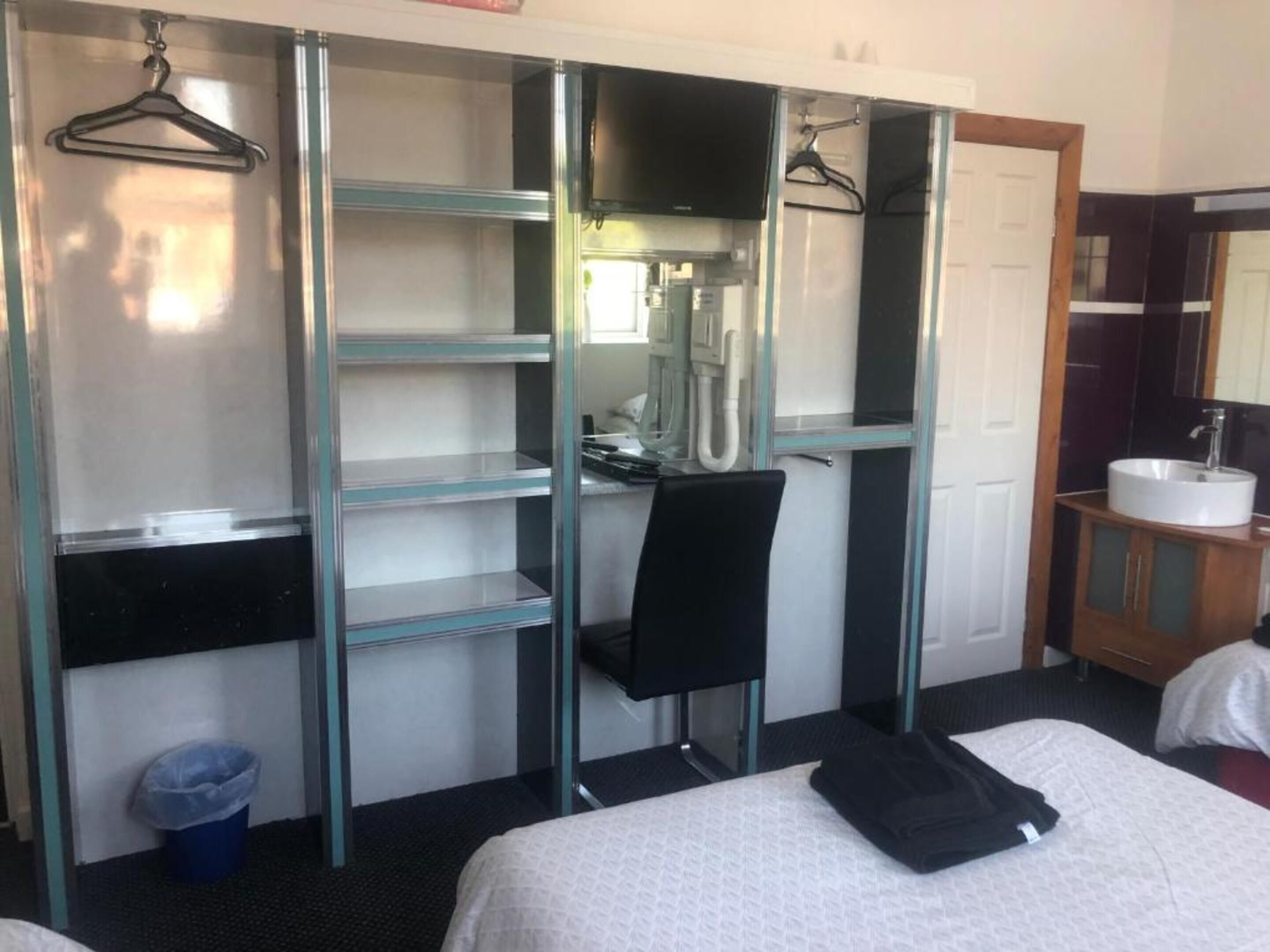 A hotel room with a bed, a desk, a chair, a wardrobe, a bathroom with a sink, and a mirror.