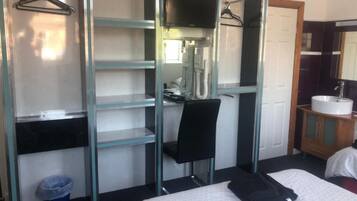 Een hotelkamer met een bed, een bureau, een stoel, een kledingkast, een badkamer met een wastafel en een spiegel.