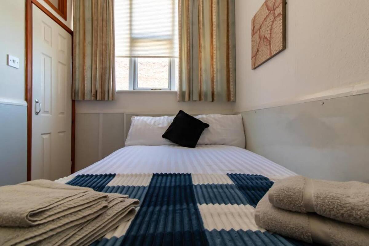 A neatly made bed with a blue and white striped blanket, a black pillow, and two folded towels on the side.