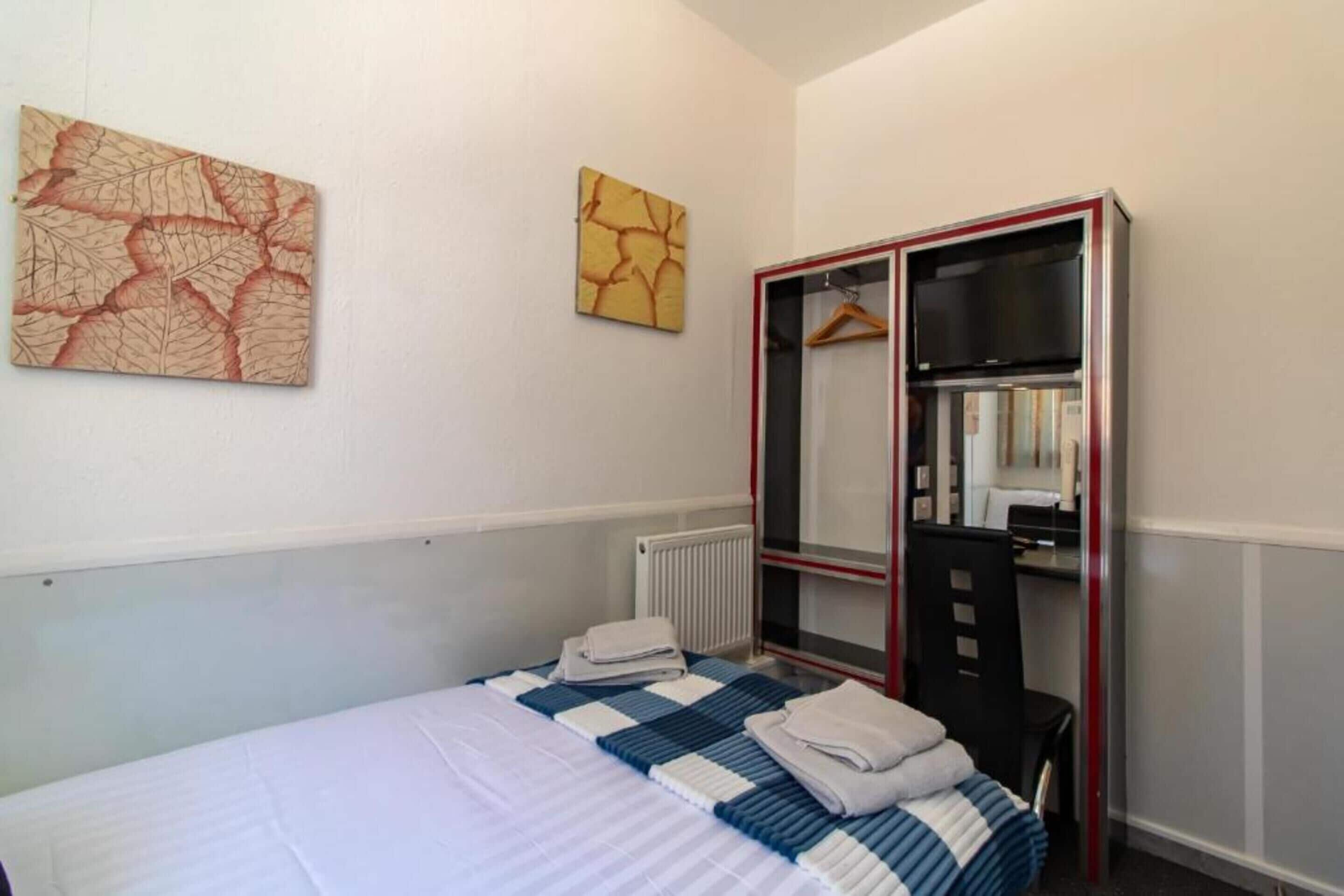 A hotel room with a bed, a wardrobe, a mirror, and two wall art pieces.
