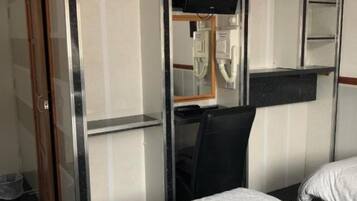 A hotel room with a bed, a desk with a computer, a mirror, and a wardrobe.