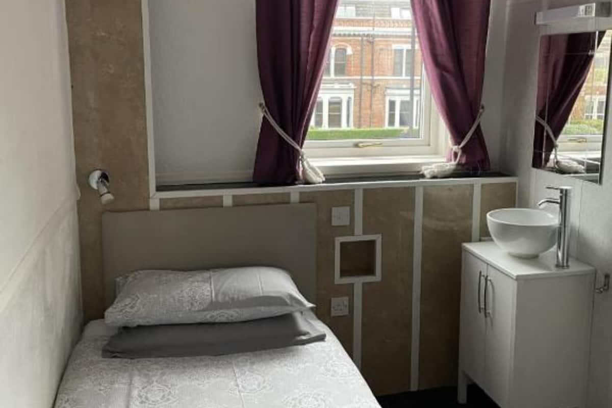A small, single-bed room with a window, a mirror, and a sink.