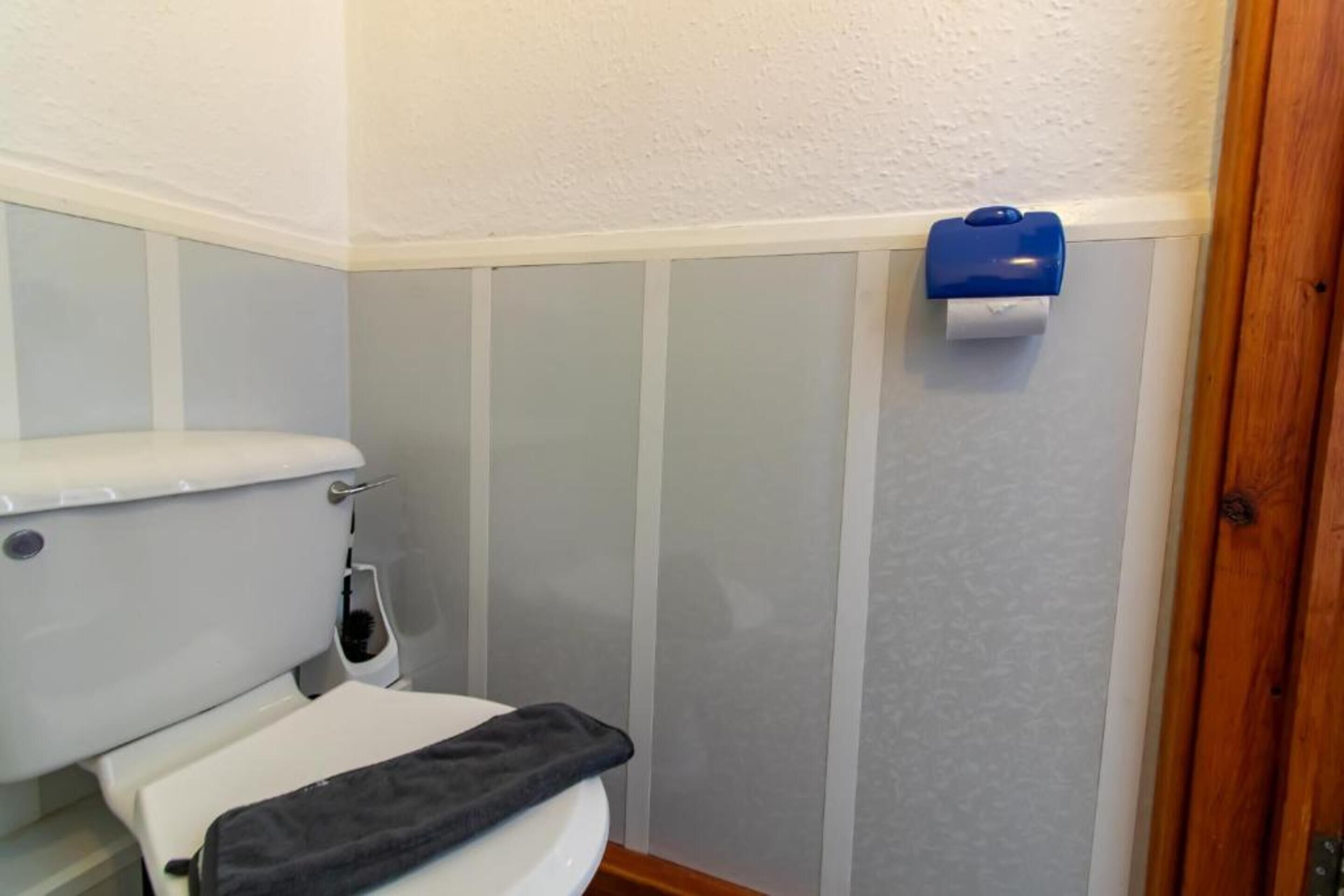 Un baño con inodoro, un secamanos azul y una pared blanca.