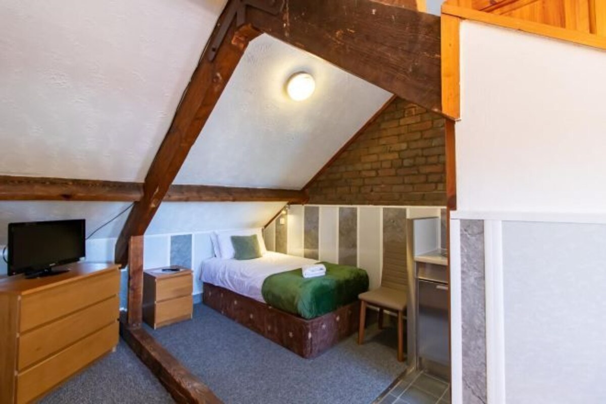 Une chambre avec un plafond de style industriel, un lit, une commode, un téléviseur et une petite table.