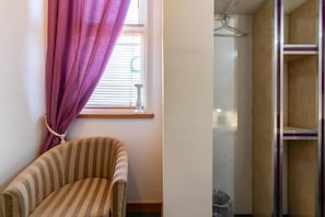 Een kamer met een gestreept fauteuil, een raam met paarse gordijnen en een douche met een witte douchegordijn.