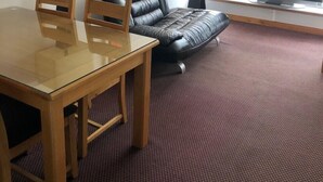 Ett hotellrum med ett matbord i trä, två stolar, en svart lädersoffa, en tv och ett fönster med utsikt.
