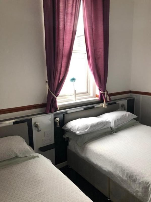 Una habitación con dos camas individuales, una ventana con cortinas moradas y un radiador sobre las camas.