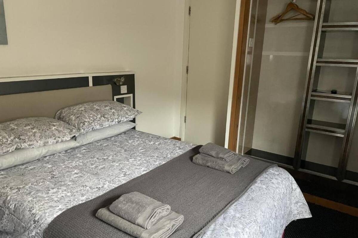 A neatly made bed with patterned bedding, a grey blanket, and folded towels.