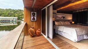 A bedroom with a large bed, wooden flooring, and a view of a river. - Uiara Amazon Resort (Manaus)