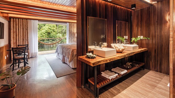 A modern bathroom with wooden paneling, a large mirror, two sinks, and a wooden vanity. - Uiara Amazon Resort (Manaus)