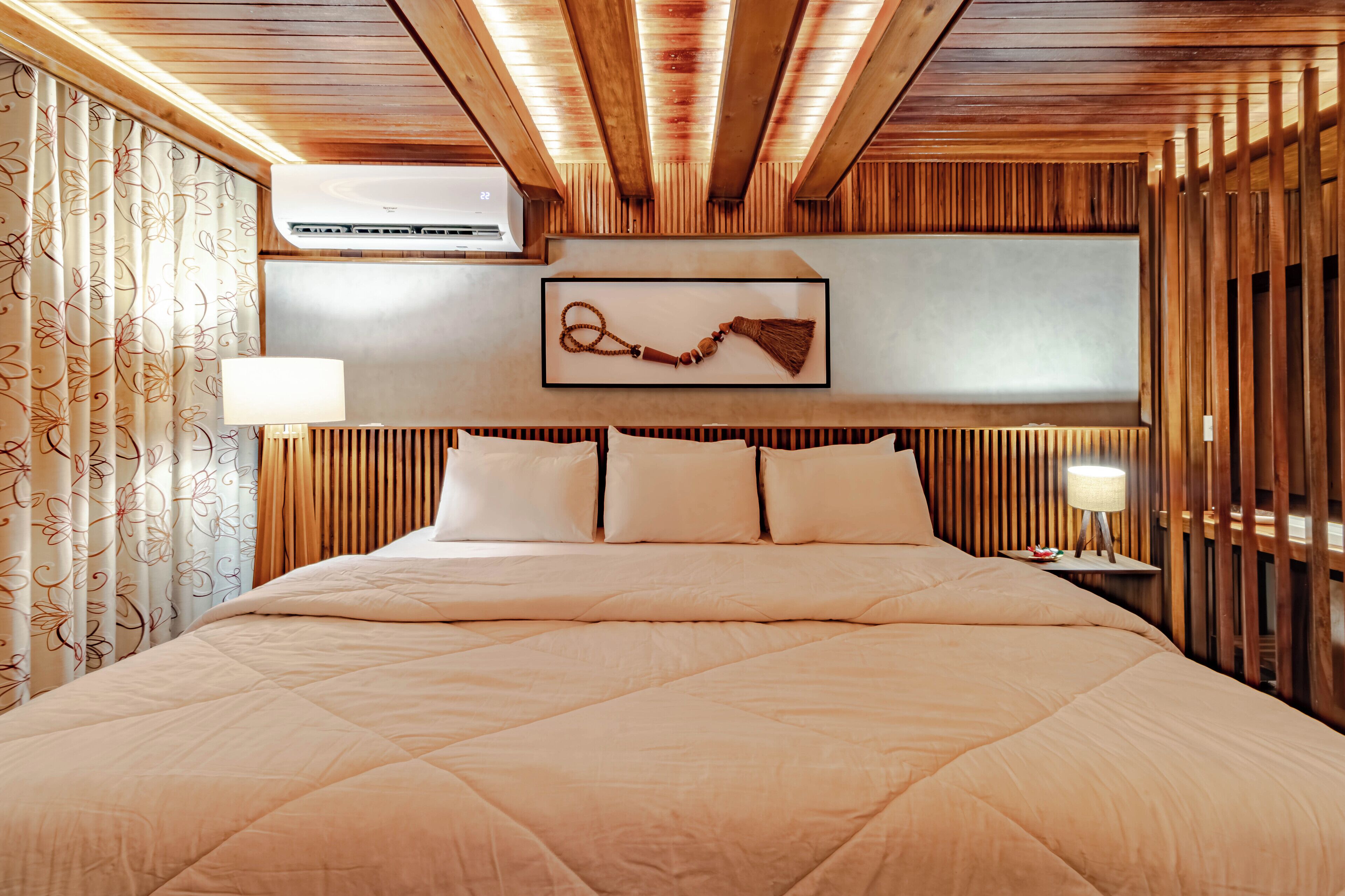 A hotel room with a large bed, wooden paneling on the walls, a mounted air conditioner, and a decorative wall piece.