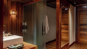 A modern bathroom with wooden paneling, a glass shower enclosure, and a wooden vanity with a sink and decorative items. - Uiara Amazon Resort (Manaus)