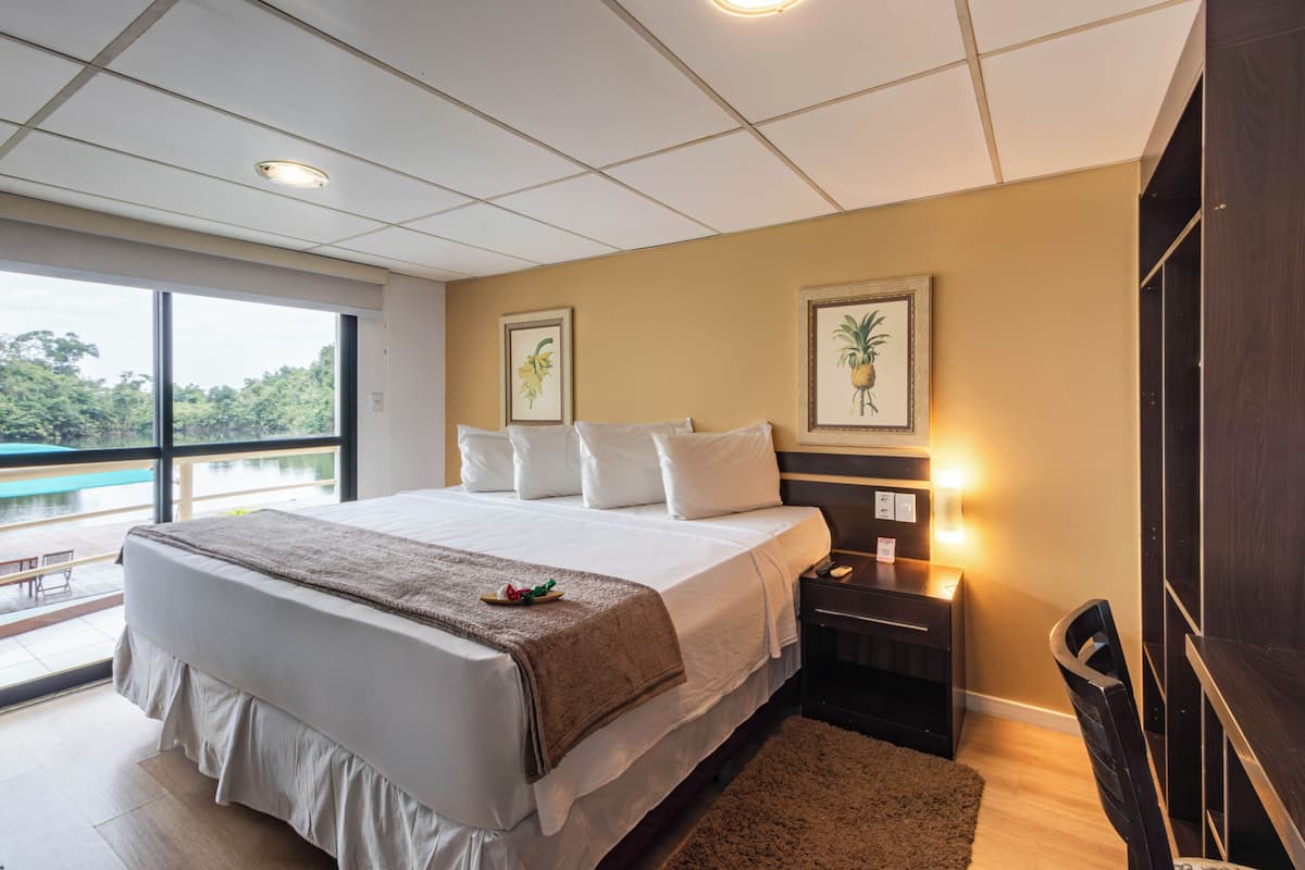 A hotel room with a large bed, a nightstand, a desk, and a view of a pool.