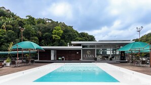 A swimming pool with a wooden deck, surrounded by outdoor seating and umbrellas, in front of a building labeled "UIARA AMAZON RESORT". - Uiara Amazon Resort (Manaus)