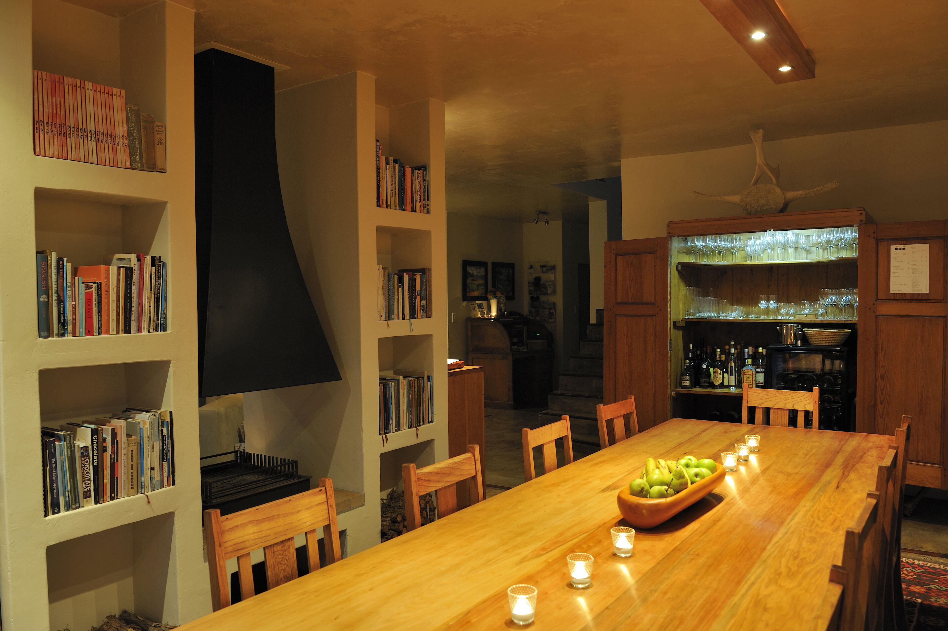 Un comedor con mesa de madera, sillas, una estantería y una zona de bar con vasos y botellas.