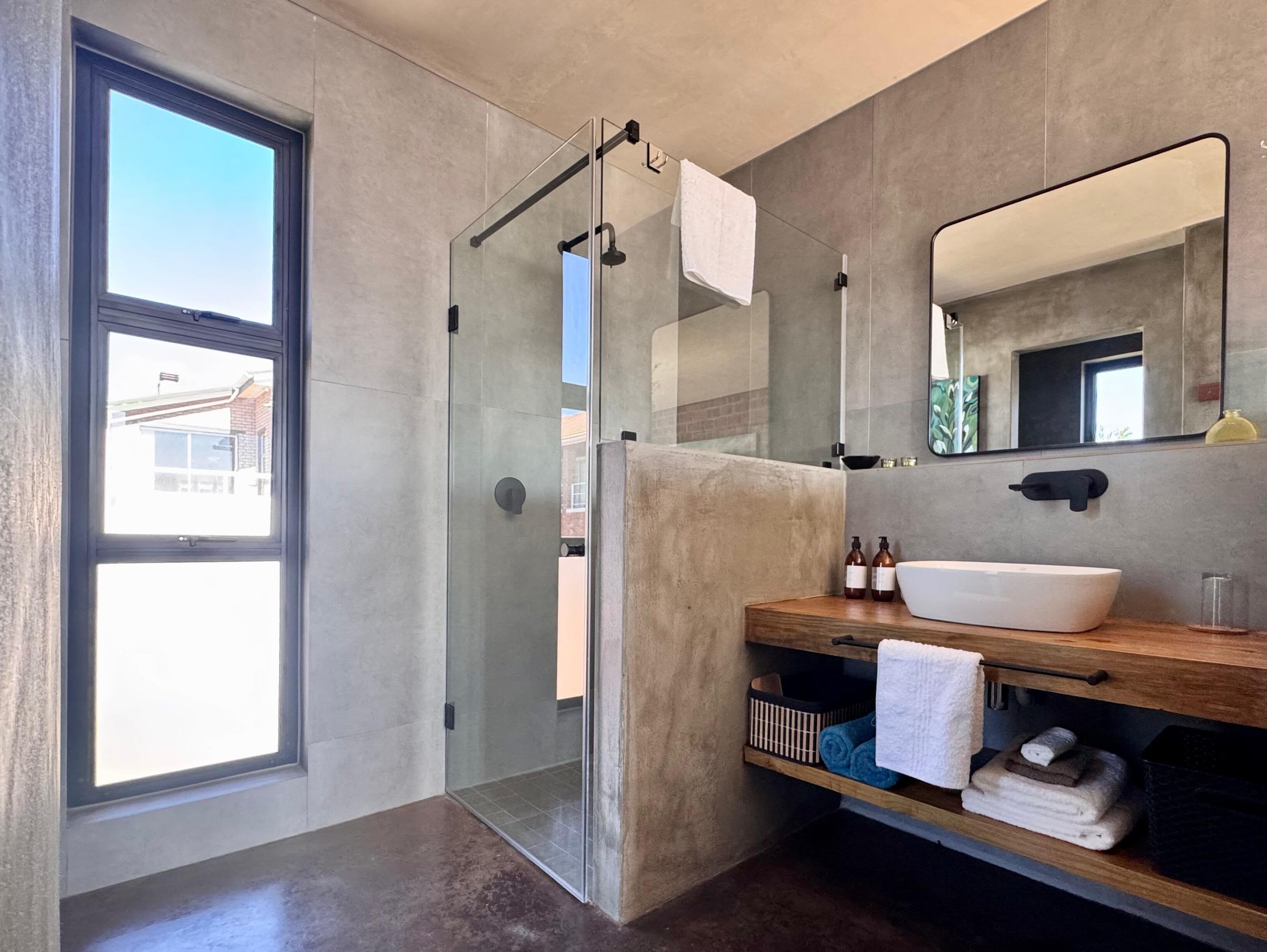 A modern bathroom with a glass shower enclosure, a large mirror, and a wooden vanity with a white sink.