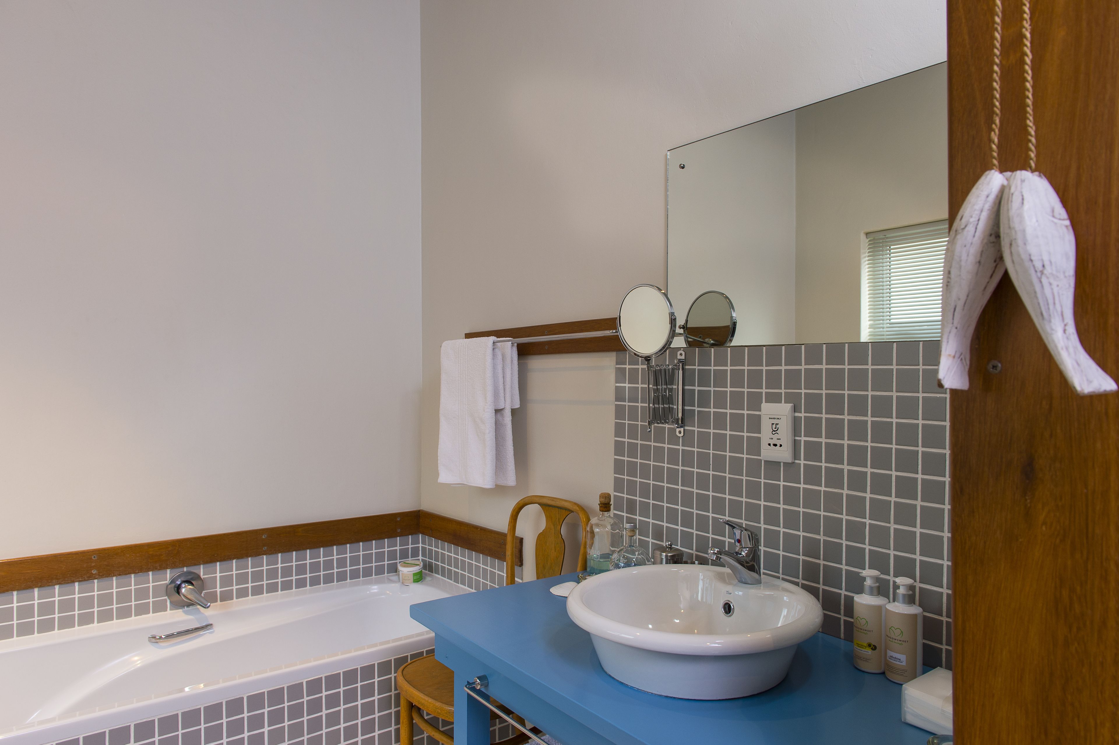 A bathroom with a bathtub, a sink, a mirror, and a wooden chair.