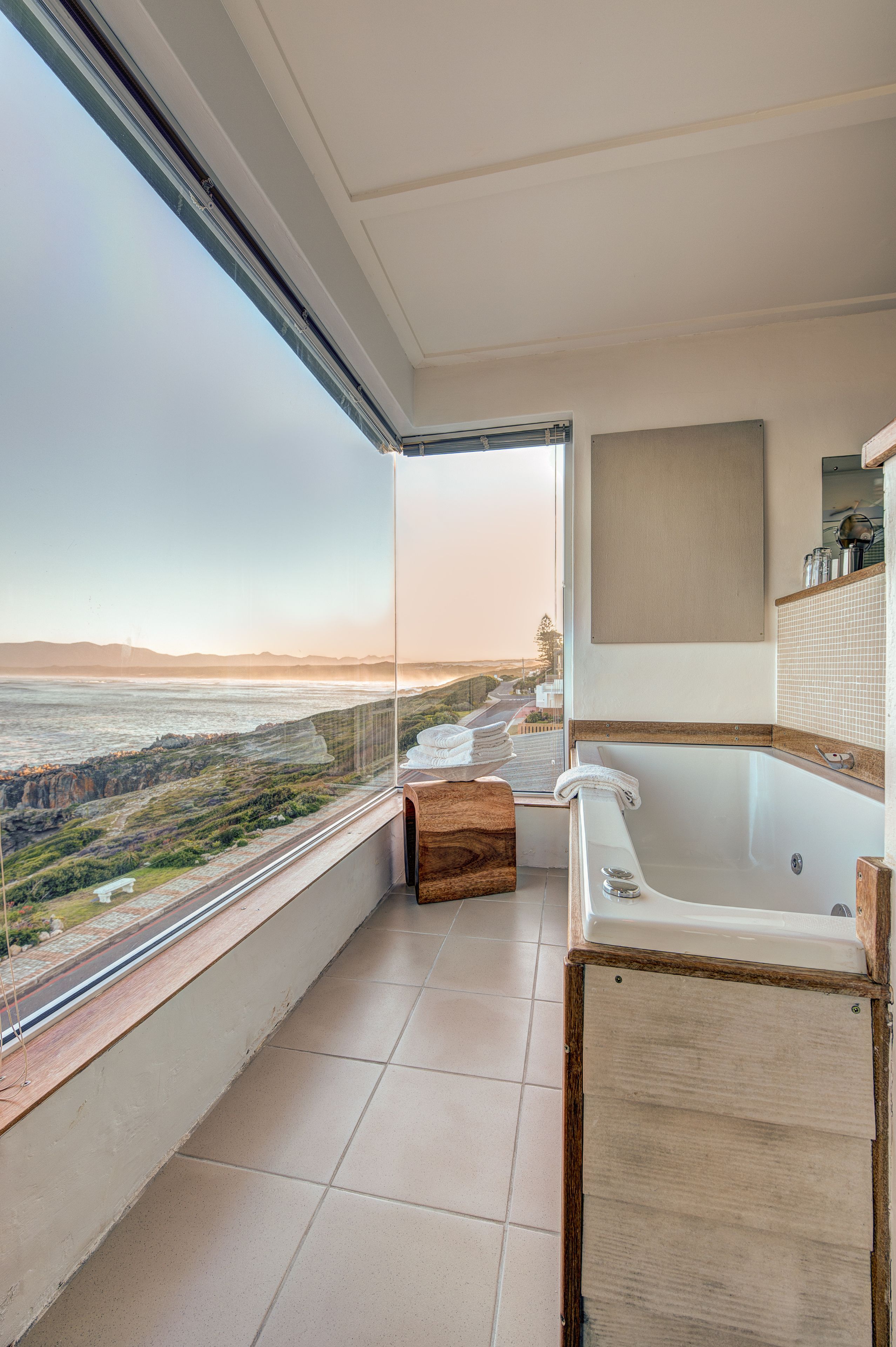 A modern bathroom with a large bathtub, a wooden bench, and a view of the ocean.